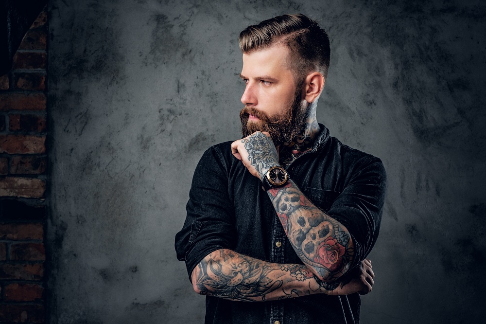 Чоловік з гарною зачіскою, доглянутою бородою та з татуюваннями на руках